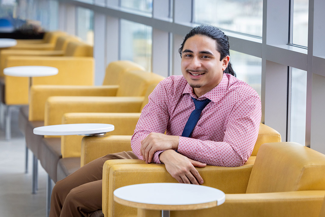 'Person smiling while seated in a modern lounge area with mustard chairs and large windows.'